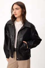 Chaqueta de cuero sintético negro con textura granulada, corte oversize, cuello camisero, cierre frontal con botones a presión, bolsillos frontales con solapa y charreteras en los hombros.