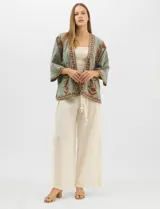 Cardigan tipo kimono de color verde con bordados florales en tono marrón a lo largo de los bordes frontales y en las mangas. Presenta un corte amplio y fluido con mangas tres cuartos.