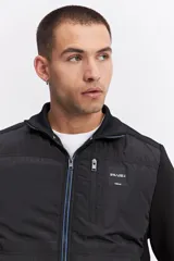 Campera de estilo deportivo con cierre frontal, confeccionada en una combinación de nylon y algodón. Presenta un diseño con paneles texturizados en las mangas, cuello alto y un parche decorativo con coordenadas en el pecho.