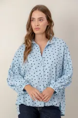 Camisa de corte oversize y diseño holgado, color celeste con estampado de pequeños corazones negros. Presenta cuello clásico, cierre frontal con botones y mangas largas abullonadas con puños ajustados.