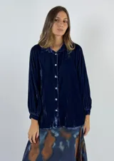 Camisa azul marino de terciopelo de viscosa, con cuello camisero, cierre frontal con botones y mangas largas con puños elásticos.