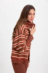 Campera de punto holgada con cuello tipo chomba y cierre frontal oculto. Presenta un diseño de rayas horizontales en tonos marrón, rojo y crema, con puños y ruedo acanalados. Incluye un parche bordado en la manga izquierda.