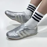 Championes Adidas modelo Taekwondo, color plateado metalizado con las tres tiras características en blanco. Presentan un diseño de perfil bajo, sin cordones visibles y suela de goma fina.