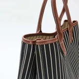Bolso tipo tote de tela a rayas verticales blancas y negras, con detalles de cuero sintético color suela en la base, manijas y bordes.