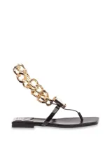 Sandalia tipo ojota color negro con base cuadrada y tira de dedo. Decoración con cadena dorada gruesa y aplique de strass cuadrado.