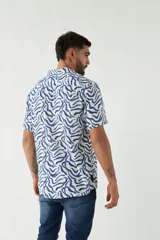 Camisa de manga corta con cuello cubano, confeccionada en viscosa con estampado de hojas en tonos azules. Presenta cierre frontal abotonado y corte slim.