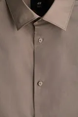 Camisa de hombre color marrón claro, de corte slim fit, con cuello italiano, tapeta lisa y canesú en la espalda. Tiene mangas largas con tapeta y botón, puños ajustables con botón y bajo ligeramente redondeado.