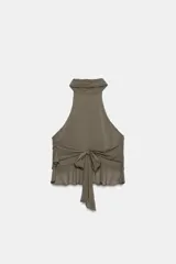 Top de cuello halter color blanco, con múltiples volantes en cascada en todo el frente y la espalda descubierta con cierre de botones y lazada en el cuello.