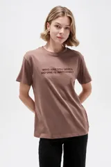 Remera de manga corta color marrón con cuello redondo y estampado frontal con la frase "Who are you when no one is watching?".