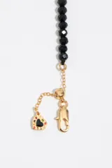 Pulsera de cuentas de cristal facetado negro combinada con finas cadenas doradas colgantes y dije con detalles esmaltados.