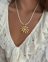 Collar con tiento trenzado blanco y dije metálico dorado con forma de sol estilizado.