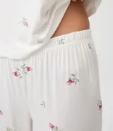 Pijama de dos piezas de viscolycra blanca con estampado floral y detalles de encaje en los hombros. Incluye una musculosa de escote redondo y un pantalón largo de corte recto.