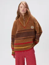 Pullover de textura aterciopelada con cuello alto y cierre frontal parcial. Presenta un diseño a rayas horizontales en tonos tierra con detalles en rojo y amarillo, puños y ruedo acanalados, y un aplique bordado en el pecho.