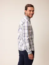 Camisa de manga larga con cuello abotonado y cierre frontal de botones. Presenta un diseño de cuadros en tonos beige, blanco y azul con líneas finas en rojo.