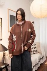 Saco tejido color chocolate con diseño inspirado en la granada, con flores y soles bordados. Presenta cierre frontal con botones, cuello redondo y puños acanalados.