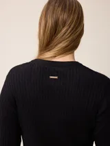 Sweater de punto con diseño de trenzas verticales, color negro, con cuello redondo, mangas largas y puños con detalle en contraste blanco. Presenta un pequeño logo bordado en el pecho.