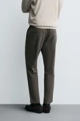 Pantalón de corte slim fit y color negro, confeccionado en tejido elástico. Cuenta con cintura elástica, trabillas, bolsillos frontales y cierre con cremallera y botón.