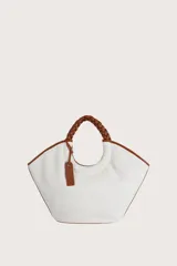 Bolso tipo tote de textura tejida en color blanco, con detalles de ribetes y asas trenzadas en color marrón. Incluye una etiqueta decorativa colgante en el mismo tono de las asas.