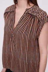 Blusa sin mangas de corte holgado, confeccionada en tela de viscosa con estampado de rayas verticales en tonos mostaza y blanco. Presenta cuello en V profundo y detalles bordados en los hombros.