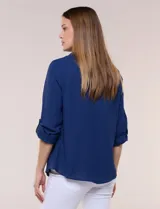 Blusa verde de calce holgado y caída fluida, confeccionada en tejido tipo crepé. Cuenta con cuello camisero con solapa, escote en V y cierre parcial al frente con tres botones metálicos. Las mangas son largas con puños abotonados.