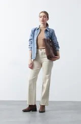 Pantalón de fit recto color beige, confeccionado en cotton spandex. Presenta costuras visibles y bordados decorativos en tono dorado/marrón claro. El ruedo del pantalón tiene un borde festoneado.