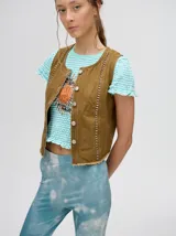 Chaleco de denim liviano con cierre frontal de botones metálicos, detalle de apliques metálicos verticales y ruedo con terminación desflecada.