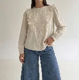 Blusa de color beige con bordados florales en el frente, detalle de volados verticales y mangas largas con puños elásticos.
