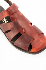 Sandalia tipo cangrejera de cuero lavado color marrón rojizo, con diseño de tiras entrelazadas, puntera cerrada y ajuste mediante correa con hebilla metálica en el tobillo.