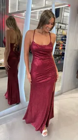 Vestido largo de fiesta color bordó con acabado brillante. Presenta escote redondo con drapeado en el busto, tirantes finos cruzados en la espalda con cierre de cordones y detalle de fruncido lateral con tajo profundo en la pierna.