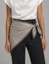 Pañuelo triangular de satén con estampado de lunares negros sobre fondo beige y borde con rayas. Presenta un diseño versátil ideal para usar como accesorio en la cintura o cuello.