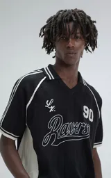 Chomba tejida de hilo color negro con punto cerrado, cuello polo con escote en V y ribetes blancos en cuello y mangas. Presenta bordados en blanco: un número "90" y la palabra "Ravers" en cursiva.