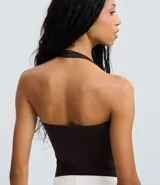 Body de poliamida color marrón oscuro, con diseño de escote halter y espalda abierta. Presenta breteles anchos que se unen alrededor del cuello y cierre inferior con botones de presión.