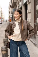 Chaqueta marrón oliva de cuero sintético, corte recto, cuello redondo y cierre frontal con cremallera. Tiene bolsillos con solapa en el pecho y mangas largas con puños abullonados.