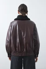 Campera de cuero sintético con acabado satinado, silueta relajada y elástico en la cintura. Presenta cuello con textura de piel sintética, cierre frontal y bolsillos laterales.