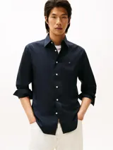 Camisa de manga larga color azul marino, confeccionada en algodón BCI con tecnología non-iron. Presenta cuello clásico, cierre frontal de botones blancos y el logo de Tommy Hilfiger bordado en el pecho.
