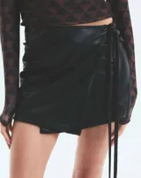 Minifalda negra de ecocuero con corte portafolio, tiro medio y lazos laterales ajustables.