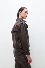 Trench corto color chocolate de cuero sintético, con doble botonadura, cuello alto y charreteras en los hombros.