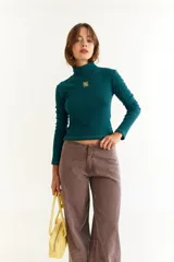 Top de manga larga con cuello alto, confeccionado en tejido de lycra y algodón. Presenta costuras a contratono, bordado central en el pecho, aberturas laterales en el ruedo y diseño con dedal en las mangas.