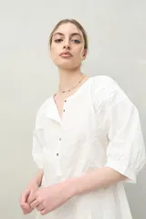 Vestido corto negro con bordado floral blanco, escote redondo con abotonadura frontal y mangas 3/4 abullonadas con pliegues en los hombros.