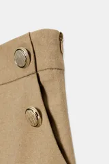 Pantalón tipo culotte de tiro alto, con pernera ancha y corta. Presenta detalles de botones dorados decorativos en la parte frontal y cierre lateral con cremallera oculta.