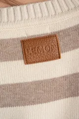 Sweater de punto con diseño a rayas horizontales en color negro y crema. Presenta cuello redondo, mangas largas con puños acanalados y un detalle de borde en tono bronce metalizado en el ruedo y los puños.