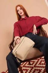 Bandolera de diseño rectangular en color suela, confeccionada en material sintético. Cuenta con un asa superior fija, correa larga ajustable y extraíble, y dos bolsillos frontales con cierre metálico, uno de ellos con diseño superpuesto. Presenta el logo de la marca grabado en el frente.