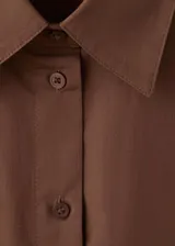 Camisa de algodón color marrón, de diseño recto, con cuello camisero, manga larga con puños abotonados y cierre delantero con botones.