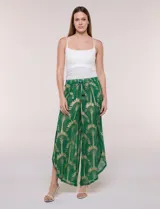 Pantalón palazzo verde de gasa con sutil transparencia y estampa metalizada dorada. Presenta cintura elastizada con cordón ajustable terminado en borlas y diseño de piernas anchas cruzadas en el frente con terminación de puntilla en los bordes.