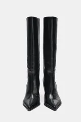 Bota de caña alta y ancha confeccionada en piel, con diseño de punta fina y tacón alto tipo aguja. Presenta costuras decorativas a lo largo del cuerpo y un diseño de calce fácil.