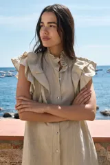 Vestido corto de lino color blanco, con cuello alto fruncido, volados marcados en los hombros y cierre frontal con botones.