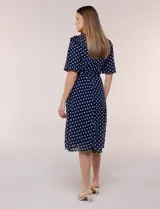 Vestido midi azul marino con estampado de lunares blancos, confeccionado en gasa semitraslúcida. Tiene escote redondo, mangas cortas acampanadas con volantes en los hombros, lazo ajustable en la cintura y falda con vuelo y forro interior.