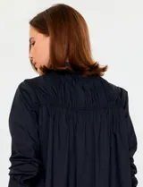 Camisa blanca de manga larga con cuello clásico y cierre frontal de botones. Presenta detalles bordados florales tono sobre tono en la zona de los hombros y el pecho.