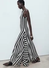 Vestido largo de punto fino con diseño evasé, cuello caja y tirantes anchos. Presenta un estampado de rayas verticales en blanco y negro y un bajo asimétrico.