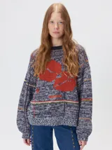 Sweater de punto con diseño geométrico y gráfico frontal en color rojo. Presenta cuello redondo, mangas largas holgadas y un ajuste suelto.